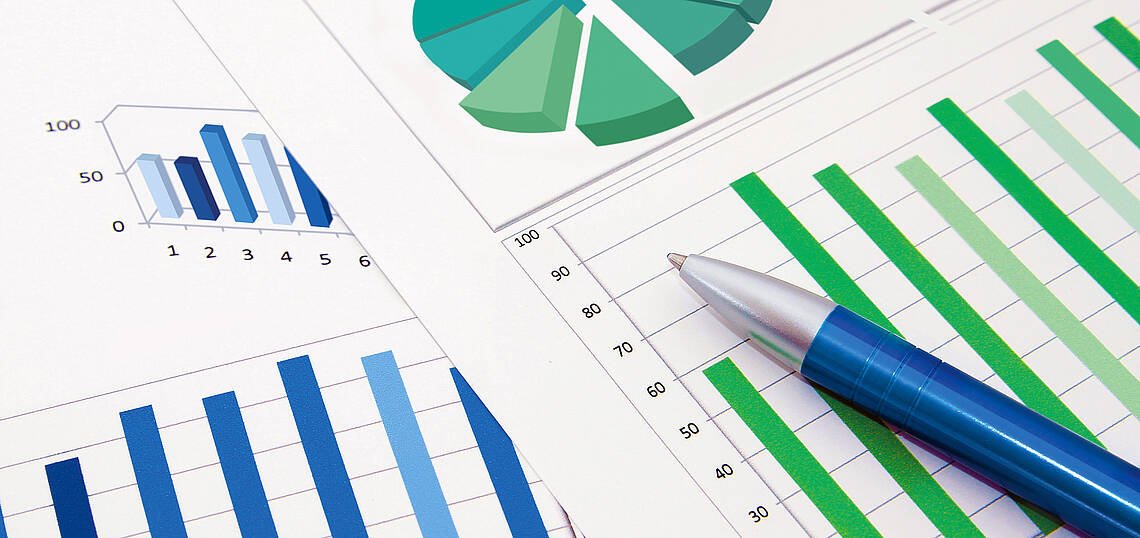 Kopfzeile „Statistiken – Branchenzahlen“ Kugelschreiber auf zwei Blättern mit Kreis- und Balkendiagrammen