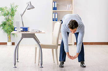 Büromitarbeiter, der an seinem Arbeitsplatz Dehnübungen macht