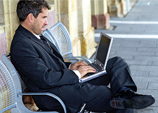 Ein Geschäftsmann wartet auf dem Bahnsteig auf den Zug und arbeitet an einem Laptop.